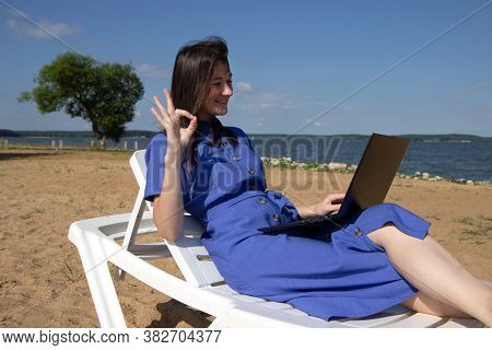 Girl Greeting During Videocall On Laptop Sitting In On The Beach. Freelancer And Blogger Participate
