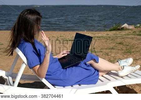 Girl Greeting During Videocall On Laptop Sitting In On The Beach. Freelancer And Blogger Participate