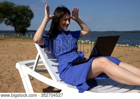 Girl Greeting During Videocall On Laptop Sitting In On The Beach. Freelancer And Blogger Participate