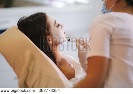 Hands Of Cosmetology Specialist Applying White Facial Mask Using Brush. Making Skin Hydrated And Fac