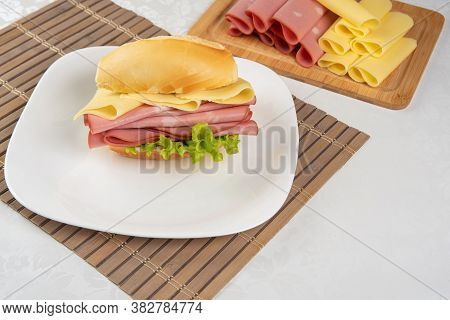 Mortadella Sandwich, Lettuce And Cheese On A White Plate On A Mat And Slices Of Mortadella And Chees