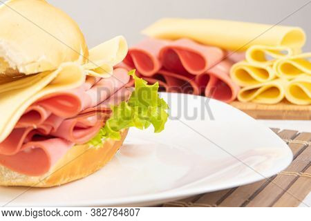 Mortadella Sandwich, Lettuce And Cheese On A White Plate On A Mat And Slices Of Mortadella And Chees