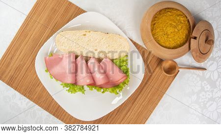 Mortadella And Lettuce Sandwich, On A White Plate And A Bamboo Mat And Pepper Sauce And Mustard On A