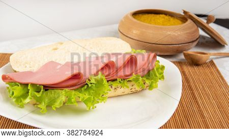 Mortadella And Lettuce Sandwich, On A White Plate And A Bamboo Mat And Pepper Sauce And Mustard On A