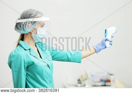 Female Doctor Or Nurse In Protective Mask At Hospital Holds Pyrometer In Hand