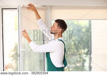 Man In Uniform Installing Roller Window Blind Indoors