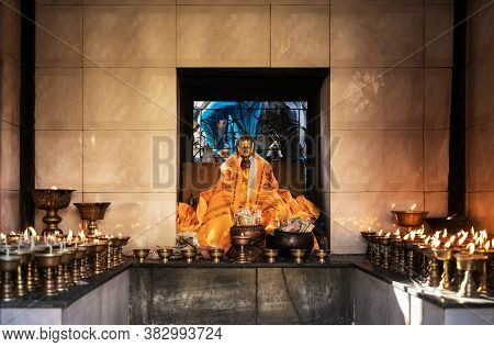 A Gilded Statue Of Buddha, Covered With A Orange Hadak, Stands On An Altar Surrounded By Lighted Oil