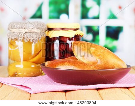 Empanadillas al horno frescos con mermelada de frutas, en la mesa de madera, sobre fondo brillante