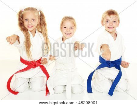 Wesoły młodych dzieci siedzą w uroczyste kimono karate pozować i Uderzyć pięścią