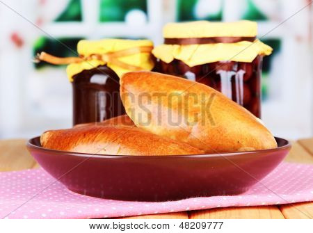 Empanadillas al horno frescos con mermelada de frutas, en la mesa de madera, sobre fondo brillante