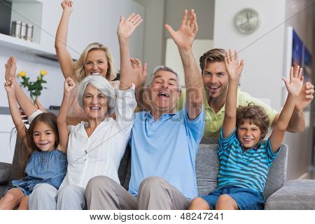 Multigenerazionali famiglia alzando le braccia insieme in salotto