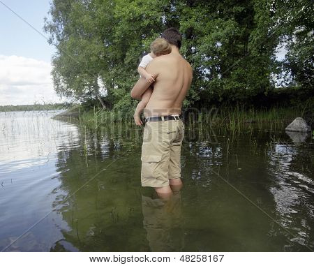 Widok z tyłu sprawny człowiek z dzieckiem stoi w spokojnym jeziorze