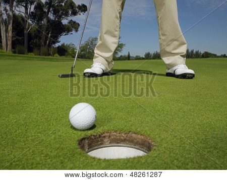 Seção de baixa de golfista masculina em verde com a bola no buraco em primeiro plano