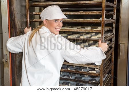 Baker tlačí stojan plný chleba do pece