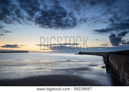 Beautiful Vibrant Sunrise Sky Over Calm Water Ocean With Lighthouse And Harbor Wall