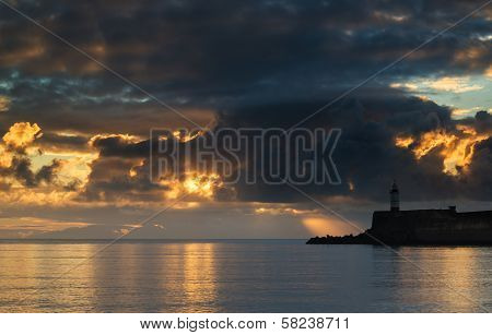 Beautiful Vibrant Sunrise Sky Over Calm Water Ocean With Lighthouse And Harbor Wall
