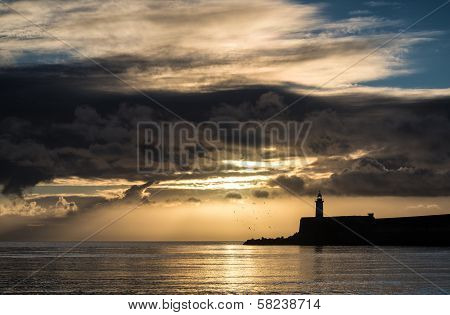Beautiful Vibrant Sunrise Sky Over Calm Water Ocean With Lighthouse And Harbor Wall