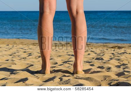 Legs Of Young Sunburnt Woman. Standing On Seashore.
