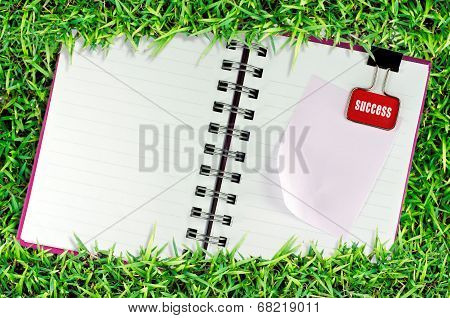blank page of note book on grass with Binder Clip
