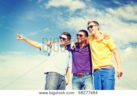 summer, holidays, vacation, happy people concept - group of male friends walking on the beach pointing finger somewhere