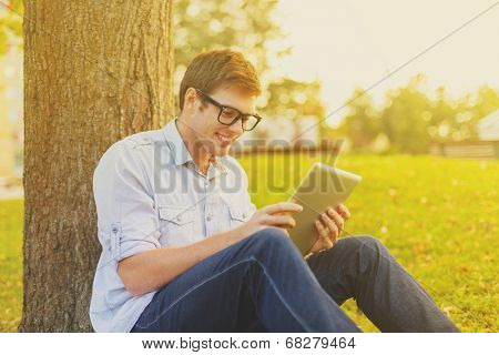 education, technology and internet concept - smiling male student in eyeglasses with tablet pc outside