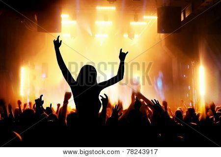 Concert, disco party. Woman silhouette with hands up in foreground and people having fun in night club