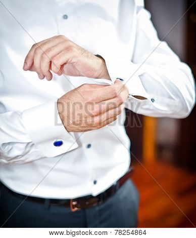 Man wears cuff-links on a shirt sleeve. A groom putting on cuff-links as he gets dressed formal wear