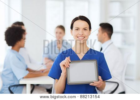 clinic, profession, people and medicine concept - happy female doctor or nurse showing tablet pc computer blank screen over group of medics meeting at hospital