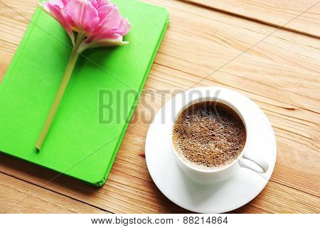 Cup of coffee with notebook and fresh flower on wooden table background