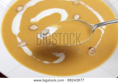 Closeup on a spoonful of traditional French butternut squash soup, garnished with cream and toasted squash seeds