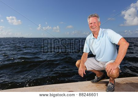 Senior man squatting by the bay