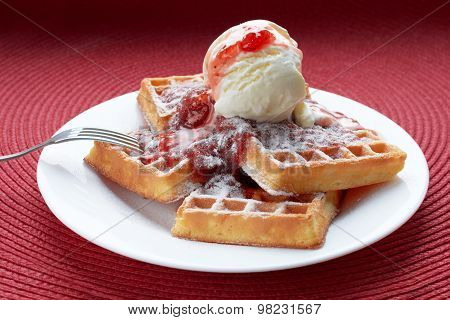 freshly baked Belgian waffles with ice cream and strawberry jam in a white plate with a metal fork on a red table