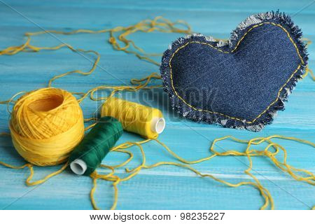 Denim heart and thread on wooden background
