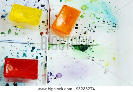 Tree bright watercolor cases on a paint box with colorful splashes