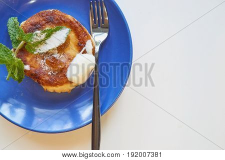 one single curd cheese pancake on a small plate with a lot of copy space. ideal breakfast. small fork, mint, sugar, raisins as delicious addition