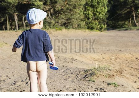 little boy standing on a sandy beach looking into the distance. Bare butt