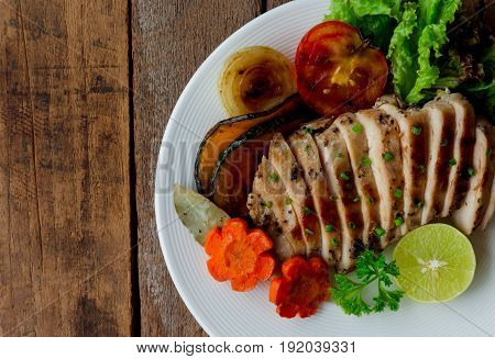 Sliced chicken breast barbecue on white plate served with grilled vegetable. Delicious chicken breast steak and salad for dinner. Homemade chicken breast barbecue on wood table for background. Chicken barbecue or pork steak.