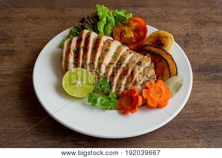 Sliced chicken breast barbecue on white plate served with grilled vegetable. Delicious chicken breast steak and salad for dinner. Homemade chicken breast barbecue on wood table for background. Chicken barbecue or pork steak.
