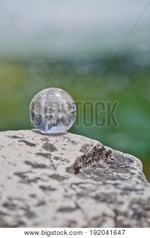 Quartz crystal ball on rock with blue green soft focused background