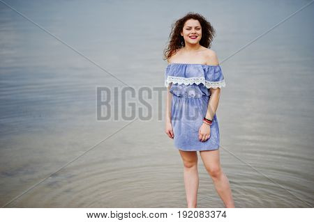 Portrait Of A Beautiful Girl With Curly Hair Wearing Marine Blye Dress Stands In The Water.