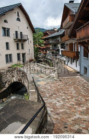 View of Megève street with little bridge, French Alps, buildings and alpine landscape, blue sky with clouds
