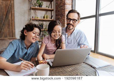 Knowledge is power. Pleasant cheerful single-parent family sitting at the table in the living room and watching an educational video on the laptop