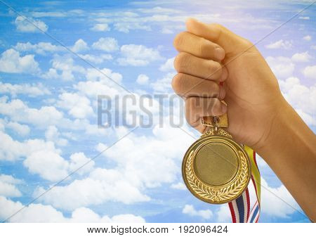 winner hand raised and holding gold medals against blue sky. success award concept