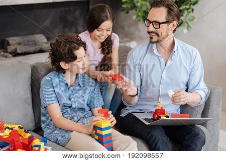 There you go. Petite little girl sitting on the sofa between her father and brother and taking a piece of an erector set from her fathers hands while her brother building a tower