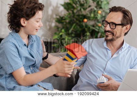 Search for appraisal. Upbeat handsome boy showing a new tower built with an erector set to his father as if wanting to hear some compliments from him
