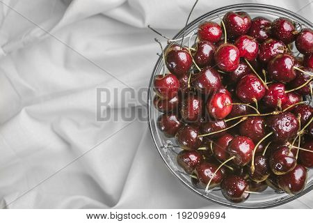 Ripe juicy cherry covered with droplets of water in a transparent bowl on a light gray background.