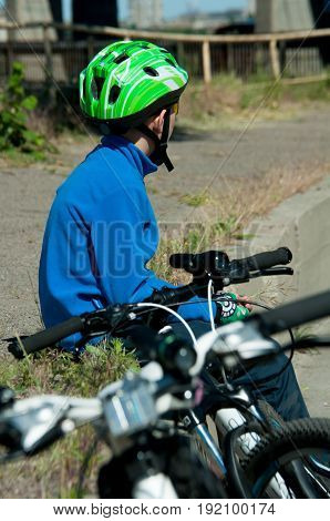The bicyclist sits in a blue sweater beside the road in a helmet next to the bike