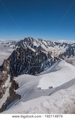 View of snowy peaks and mountaineers from the Aiguille du Midi, in French Alps Chamonix Mont Blanc, alpine mountains landscape, clear blue sky in warm sunny summer day