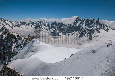View of snowy peaks and mountaineers from the Aiguille du Midi, in French Alps Chamonix Mont Blanc, alpine mountains landscape, clear blue sky in warm sunny summer day. Retouched photo