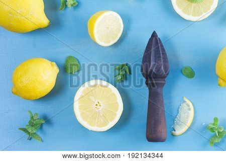 Fresh lemon citrus fruits with mint leaves and citrus reamer on blue bakground